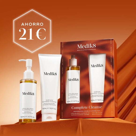 Cuatro productos de limpieza Medik8 (un frasco transparente con líquido amarillo, un tubo blanco, un frasco transparente con líquido amarillo y un tubo blanco más pequeño) dispuestos sobre un fondo naranja oscuro con textura, con una caja de producto abierta visible detrás de ellos. En la esquina superior izquierda se muestra de forma destacada un hexágono blanco con el texto AHORRO 21€-7