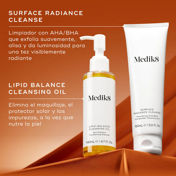 Dos productos de limpieza Medik8, un tubo blanco y un frasco transparente con líquido amarillo, colocados sobre un fondo naranja intenso. El tubo de la izquierda lleva la etiqueta «SURFACE RADIANCE CLEANSE» con la descripción «limpiador AHA/BHA que exfolia suavemente, alisa e ilumina». El frasco de la derecha lleva la etiqueta «LIPID BALANCE CLEANSING OIL» con la descripción «Disuelve las impurezas mientras nutre la piel».-hover-7